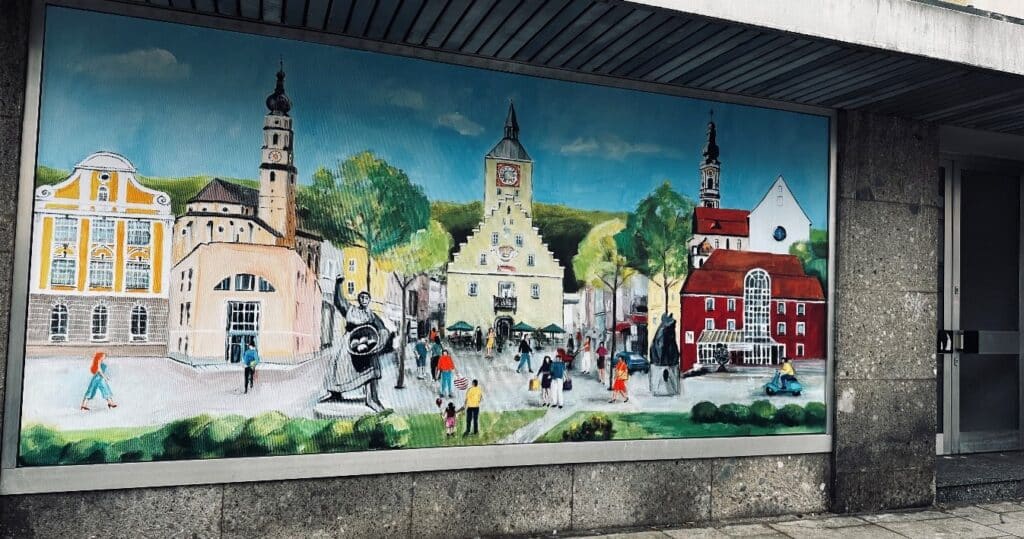 Wandgemälde mit einer belebten historischen Stadtansicht, mehreren Kirchtürmen, Häusern und Menschen im öffentlichen Raum.