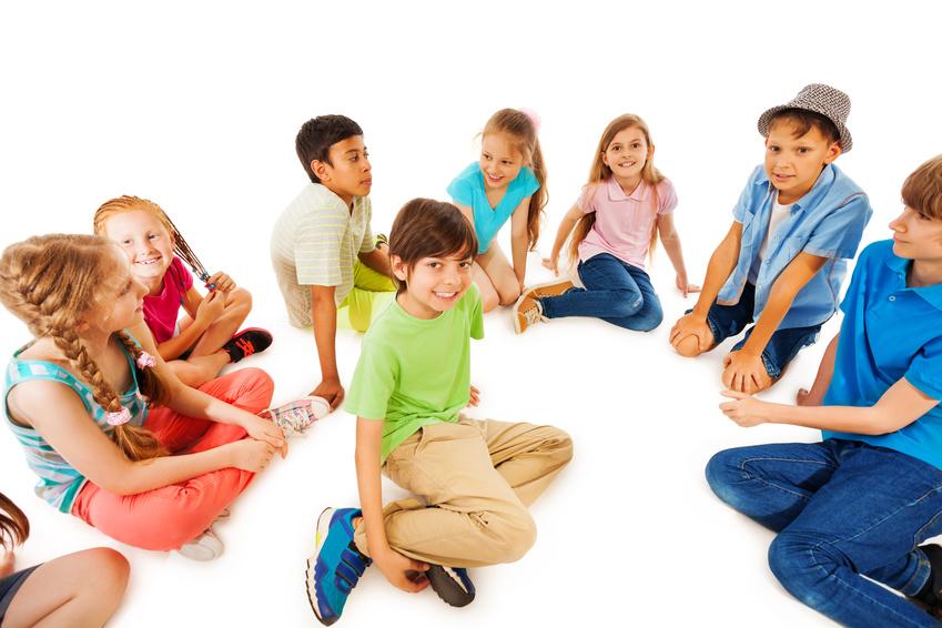 Gruppe von Kindern sitzt und kniet in einem hellen Raum zusammen.