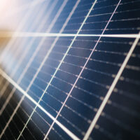 Nahaufnahme einer dunkelblauen Solarzelle mit reflektierenden Metallleitern und einfallendem Sonnenlicht.