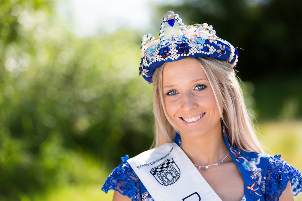 Lächelnde junge Frau mit blau-silberner Krone und blauem Kleid; über ihrer Schulter liegt eine Schärpe mit dem Wappen und Namen der Stadt Deggendorf.