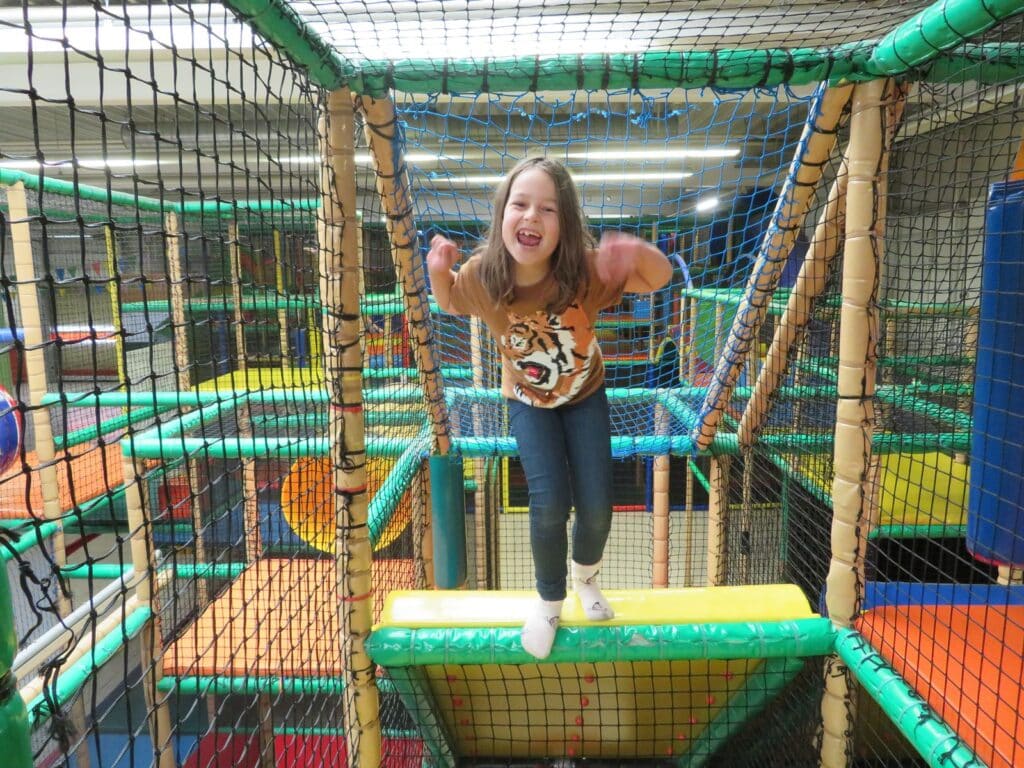 Lachendes Mädchen in einem bunten Indoor-Spielbereich mit Netzen und Kletterelementen