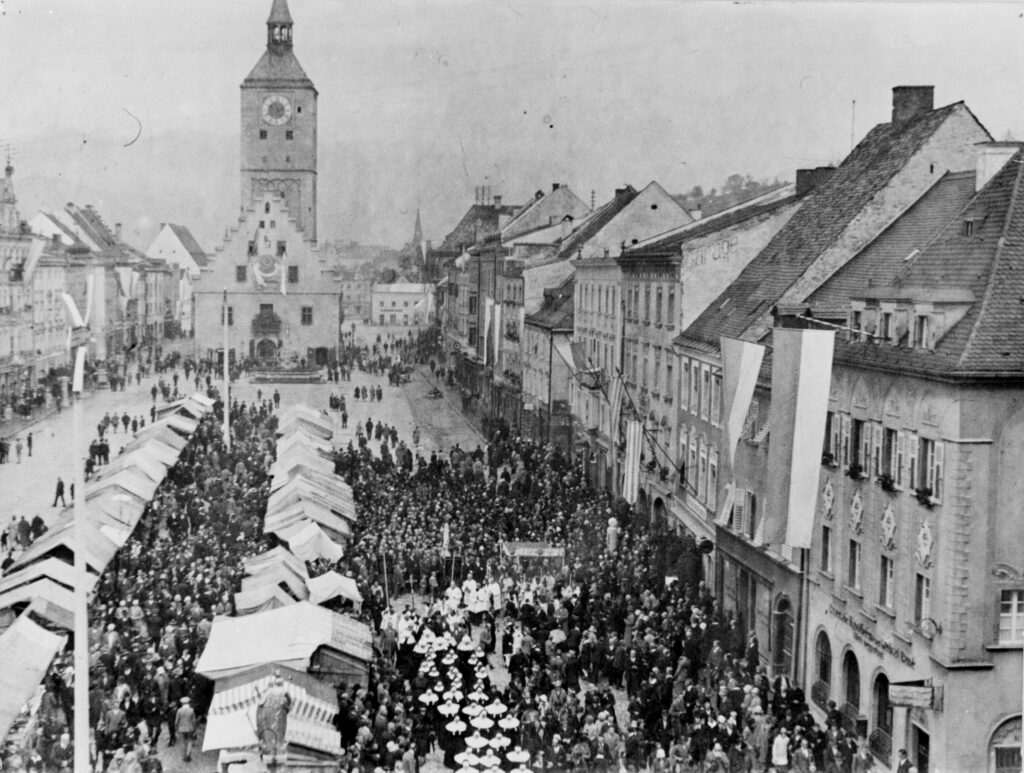Historischer Markt mit Festzug in Deggendorf Historische Schwarz-Weiß-Aufnahme eines dicht besuchten Marktplatzes mit Verkaufsständen, Menschenmenge und Festzug vor dem Stadtzentrum von Deggendorf.