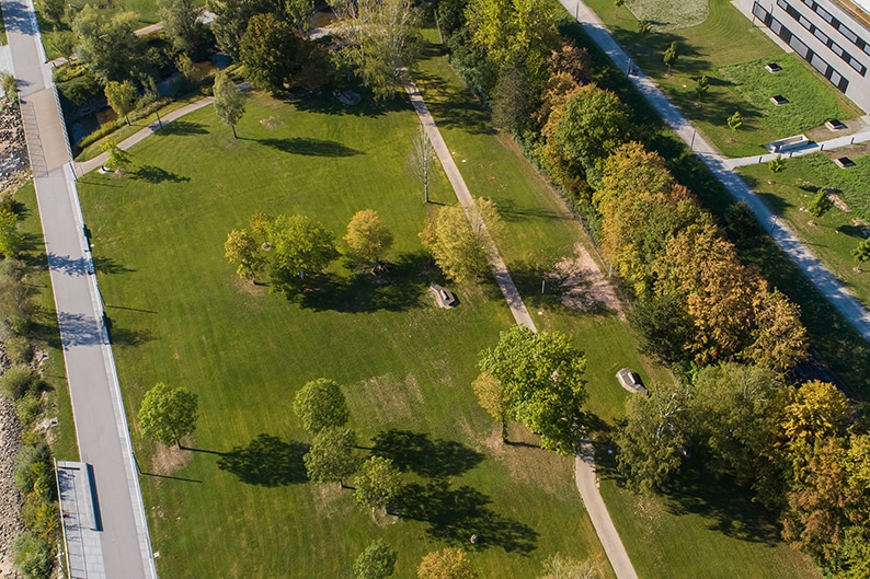 Luftaufnahme einer weitläufigen Grünanlage mit Rasenflächen, geschwungenen Wegen, Bäumen und angrenzenden Straßen in Deggendorf