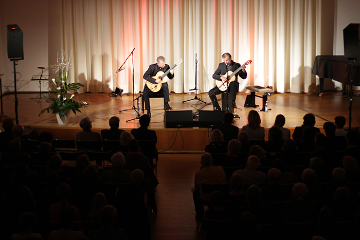 Gitarrenduo beim Konzert im Jahr 2009 Zwei Musiker spielen auf einer Bühne vor Publikum akustische Gitarren; im Hintergrund stehen Mikrofone, Lautsprecher und ein Flügel.