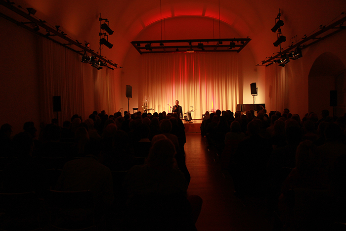 Bühnenveranstaltung im Lichtspielhaus Deggendorf 2009 Publikum bei einer Bühnenveranstaltung in einem abgedunkelten Saal mit orangefarbener Beleuchtung und einer Person auf der Bühne