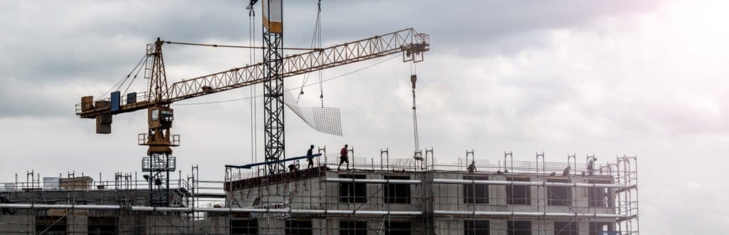Rohbau eines mehrstöckigen Gebäudes mit mehreren Baukränen unter bewölktem Himmel