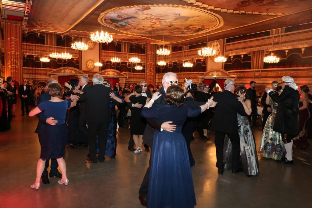 Tanzende Paare bei einem venezianischen Maskenball in einem festlich beleuchteten Saal