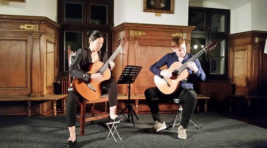 Gitarrenkonzert des Vereins in Deggendorf, Saison 2015 Zwei Gitarristinnen spielen vor holzvertäfelten Wänden auf einer Bühne; vor ihnen stehen Notenständer.