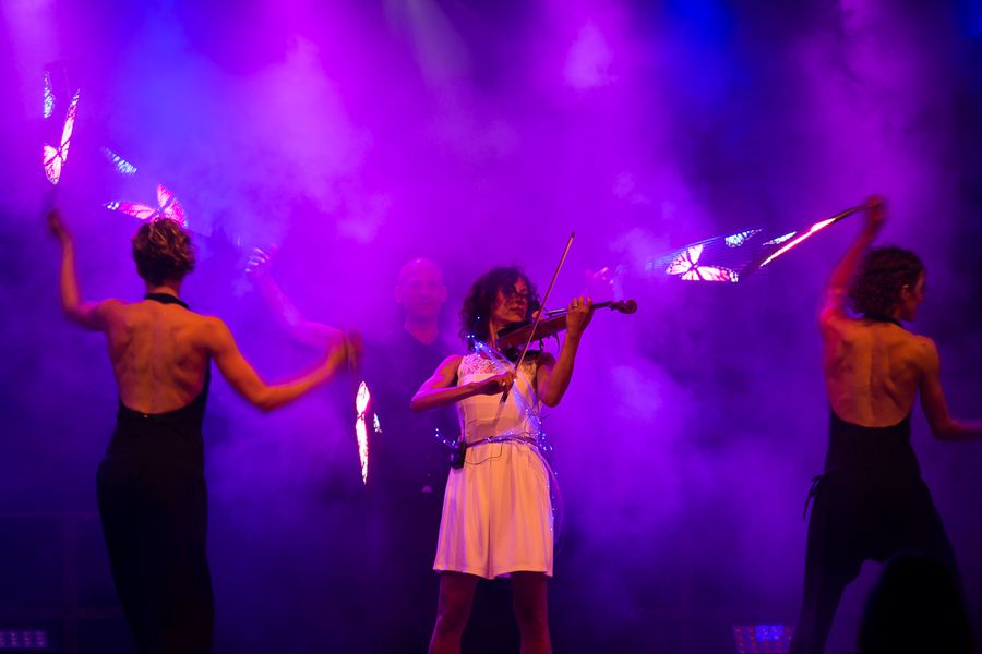 Bühnenauftritt des Vereins beim Sommerfest 2009 in Deggendorf Geigerin in hellem Kleid spielt auf einer violett beleuchteten Bühne, flankiert von zwei Tänzerinnen im Nebel.