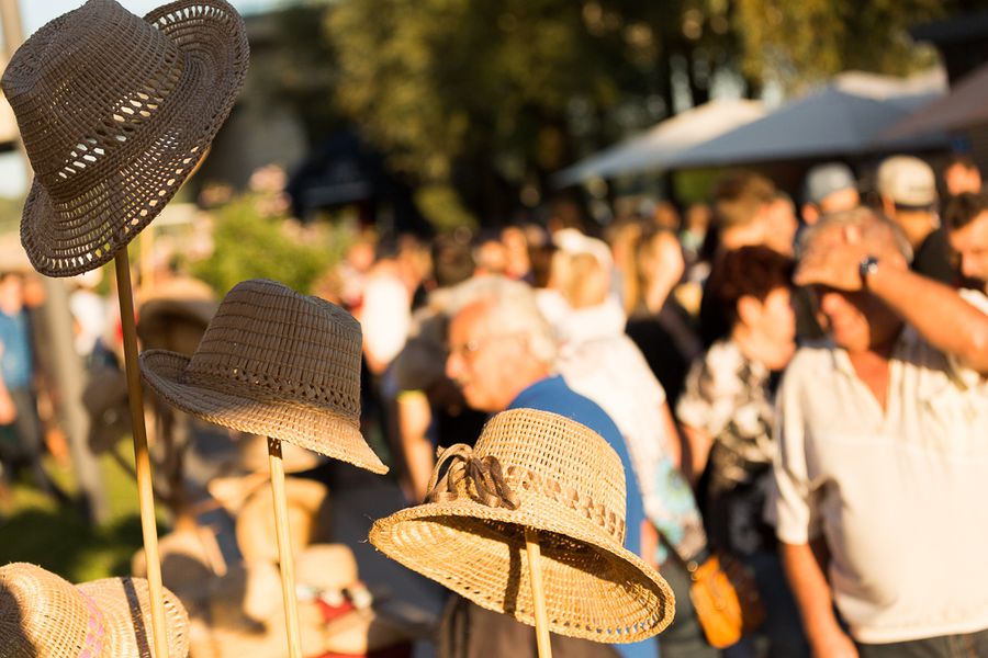 Sommerveranstaltung mit Strohhüten in Deggendorf 2009 Mehrere Strohhüte auf Ständern im Vordergrund, dahinter eine Gruppe von Menschen bei einer sommerlichen Veranstaltung im Freien.