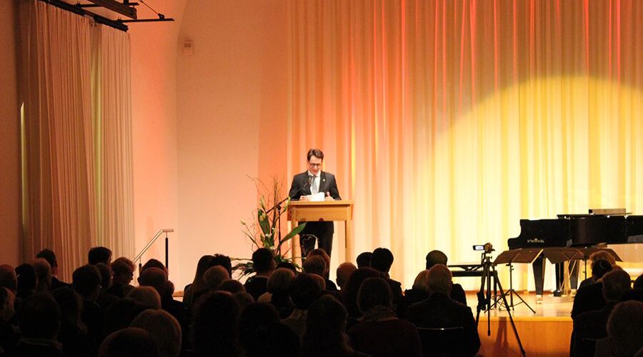 Festveranstaltung des Vereins in Deggendorf, Saison 2009 Redner an einem Pult auf einer beleuchteten Bühne vor sitzendem Publikum; rechts stehen ein Flügel und ein Mikrofonständer.