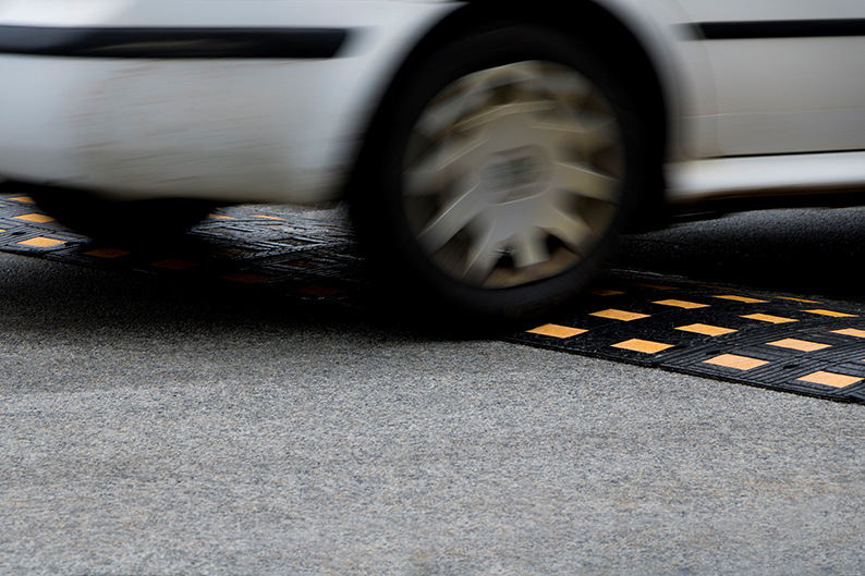 Nahaufnahme eines fahrenden weißen Autos über einer strukturierten gelben Fahrbahnmarkierung auf der Straße
