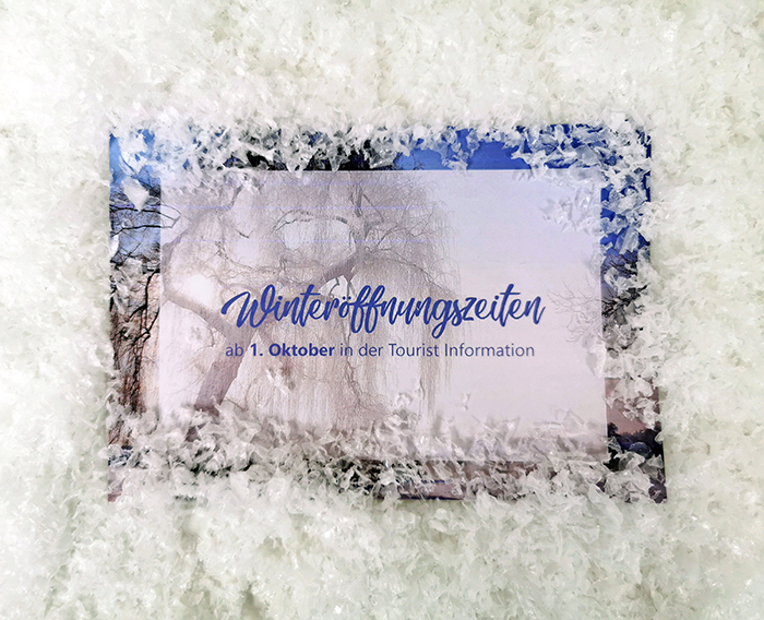 Beschilderung mit dem Hinweis „Winteröffnungszeiten ab 1. Oktober“ vor einer verschneiten Winterlandschaft