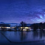 Abendstimmung am See in Deggendorf Dämmerung über einem See mit Uferpromenade, beleuchteten Gebäuden, Bäumen und Bergen im Hintergrund