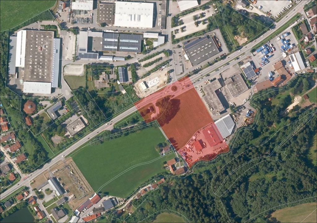 Luftaufnahme eines Gewerbegebiets in Großwalding mit rot markierter Grundstücksfläche neben einem Fußballplatz und bewaldetem Hang.