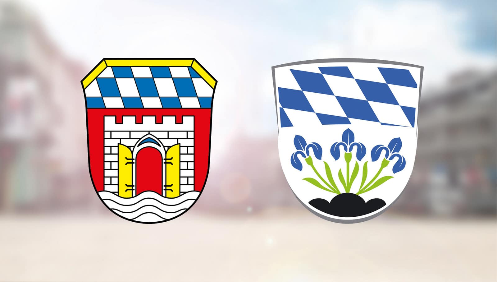 Die Wappen der Städte Deggendorf und Plattling nebeneinander vor einem unscharfen Hintergrund