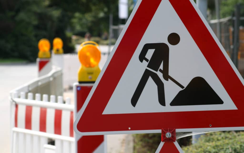 Straßensperrung wegen Baumaßnahmen in Deggendorf Verkehrszeichen mit einem arbeitenden Bauarbeiter vor einer rot-weißen Absperrung an einer Straße