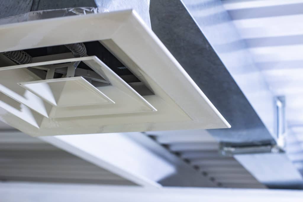 Weiße, geometrisch gestaltete Deckenverkleidung mit integrierten Leuchten und sichtbarer Gebäudetechnik
