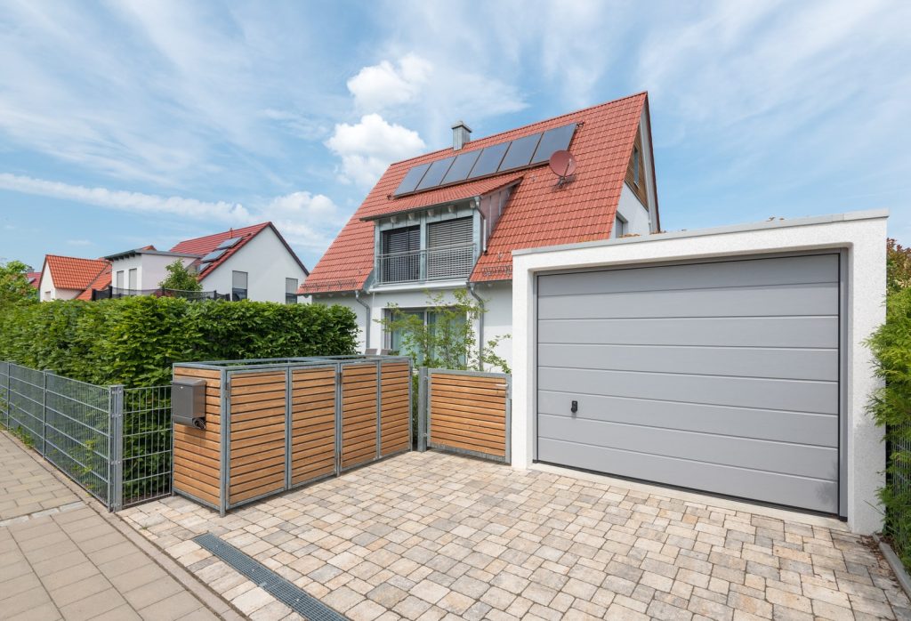 Wohnhaus mit Doppelgarage in Deggendorf Modernes Wohnhaus mit rotem Ziegeldach, Solarmodulen, Holzverkleidung und großer Doppelgarage an einer gepflasterten Einfahrt