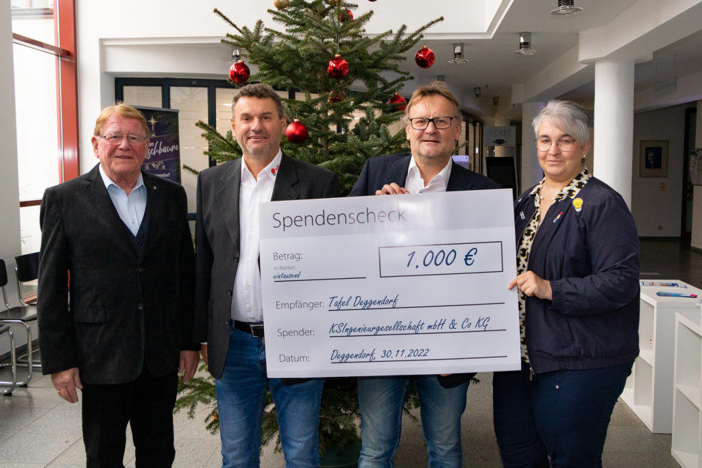 Spendenübergabe der KSI-Ing. Gesellschaft an die Tafel in Deggendorf Vier Personen präsentieren vor einem geschmückten Weihnachtsbaum einen Spendenscheck über 1.000 Euro für die Tafel.