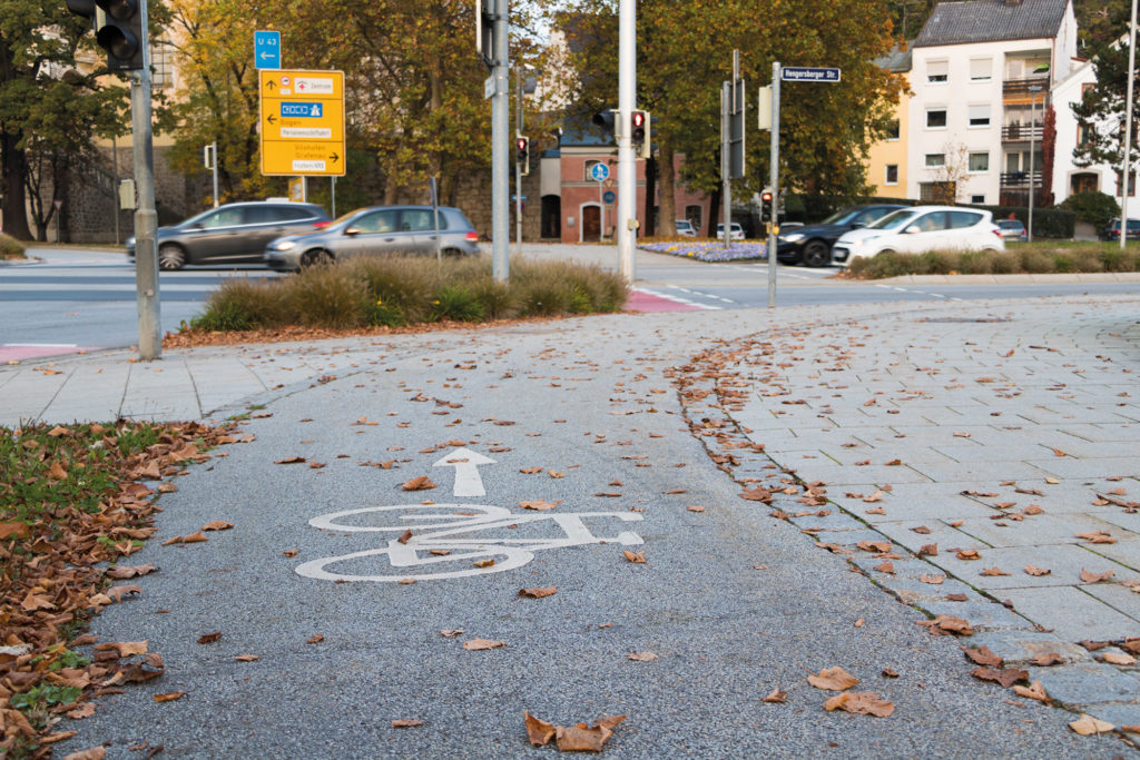 Markierte Rad- und Fußwege an einer Kreuzung in Deggendorf mit Wegweisern, Straßenverkehr und herbstlichem Laub