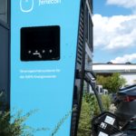 Blaues Fenecon-Werbeschild an einem Gebäude mit Darstellung eines Energiespeichersystems und Ladegerät im Vordergrund