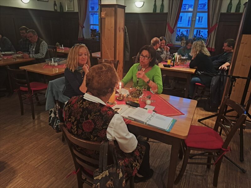 Gesellige Runde bei M23-Veranstaltung 2023 Menschen sitzen in einem Gastraum an mehreren Tischen und unterhalten sich bei Getränken und Unterlagen.