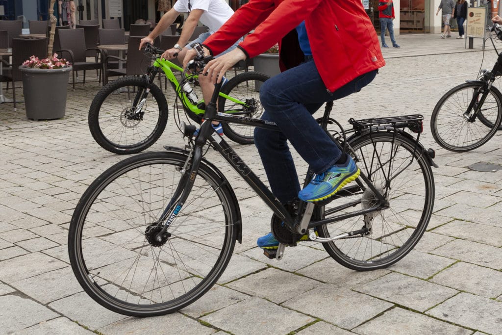 Zwei Radfahrer fahren mit Fahrrädern über einen gepflasterten Stadtplatz in Deggendorf.
