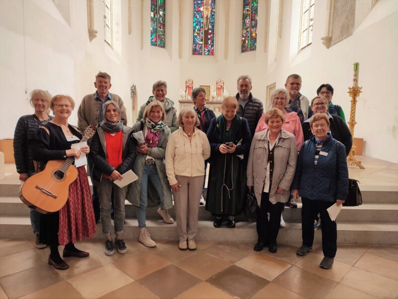 Gruppenfoto des Vereins M23 in Deggendorf Gruppe von Erwachsenen mit einer Gitarristin vor dem Altar in einer Kirche