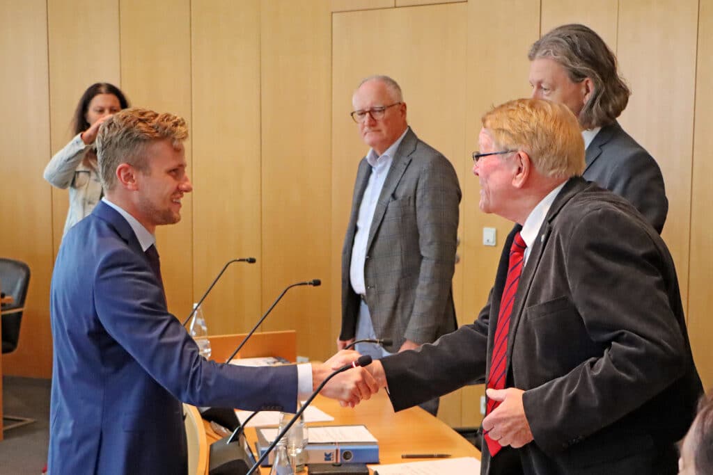 Ausschüsse des Stadtrats am 30. September 2024 Zwei Männer schütteln sich in einem Sitzungssaal des Stadtrats die Hände, während weitere Personen am Tisch stehen.