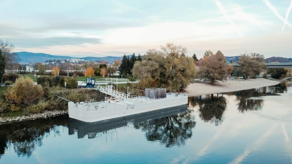 Drohnenaufnahme eines Pontons auf der Donau mit Uferbereich, Bäumen und der Landschaft bei Deggendorf im Hintergrund