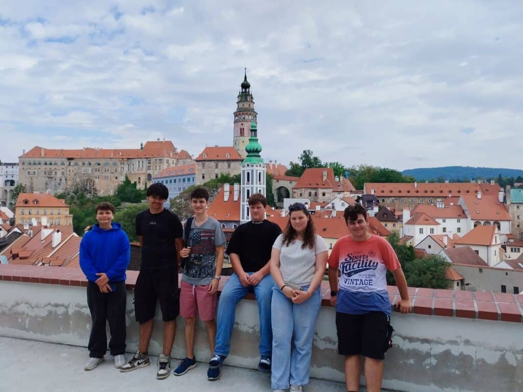 Sieben Jugendliche stehen vor der historischen Altstadt von Krumau mit dem Schlossturm im Hintergrund.