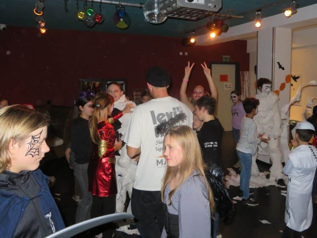 Halloween-Veranstaltung von 4You in Deggendorf 2024 Menschen in verschiedenen Halloweenkostümen feiern in einem dekorierten Veranstaltungsraum mit farbiger Beleuchtung und Diskokugel.