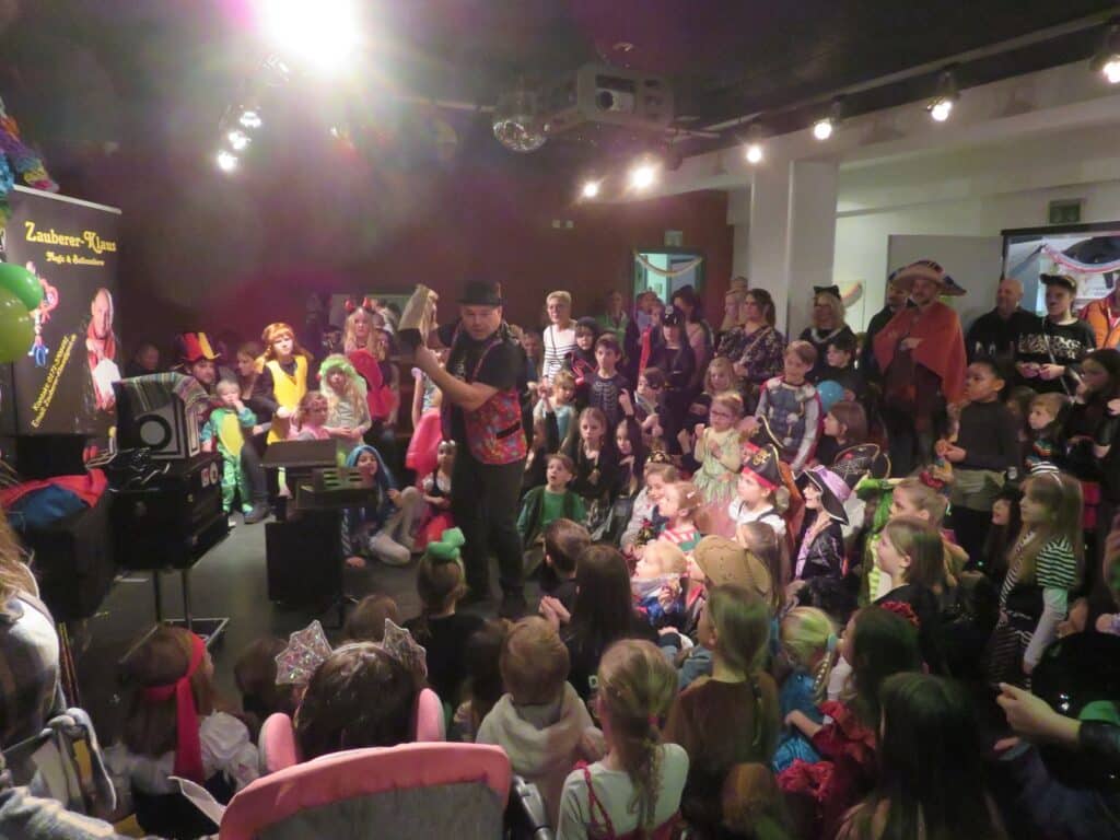 Kinder und Erwachsene in bunten Kostümen verfolgen eine Bühnenshow beim Kinderfasching im 4You.
