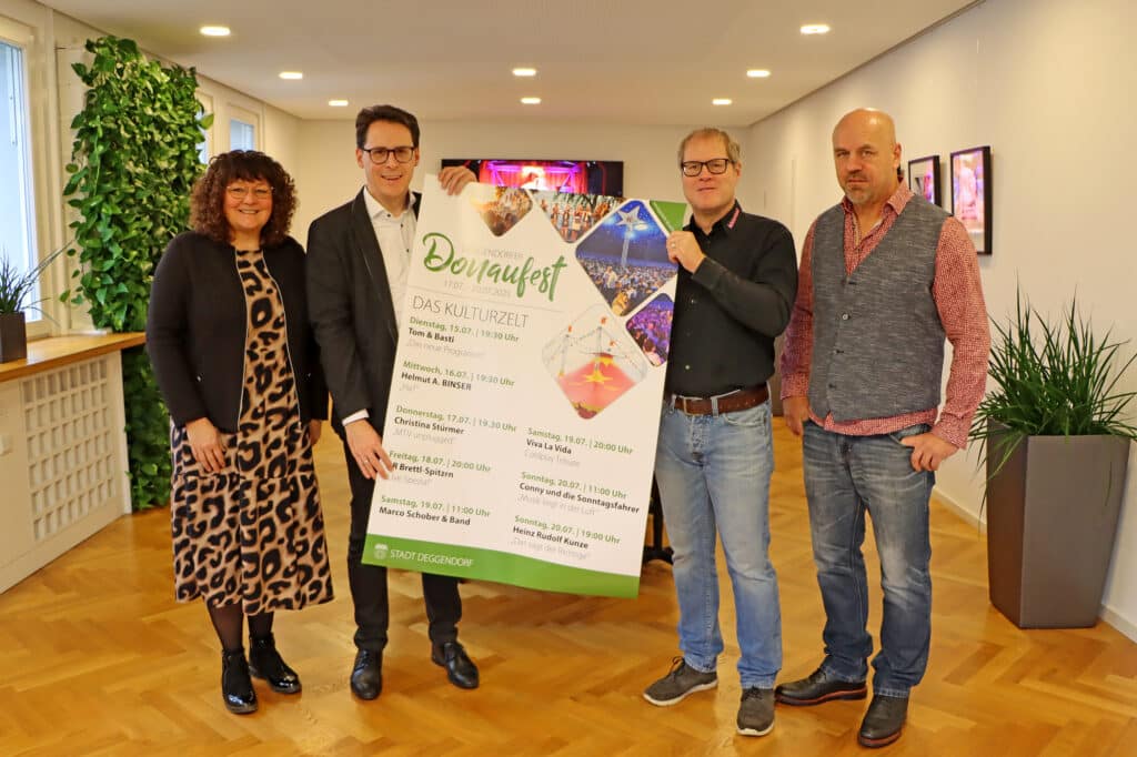 Donaufest 2025: Programmvorstellung im Kulturzelt Vier Personen präsentieren gemeinsam ein großes Plakat mit dem Programm des Donaufests 2025 in einem Innenraum.