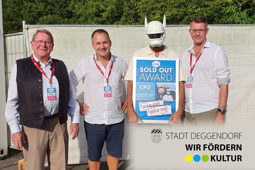 Vier Personen stehen bei einer Kulturveranstaltung neben einer Person in einem weißen Roboterkostüm, die einen „Sold Out Award“ mit dem CRO-Logo hält; im Vordergrund ist das Logo der Stadt Deggendorf mit dem Hinweis „Wir fördern Kultur“ zu sehen.
