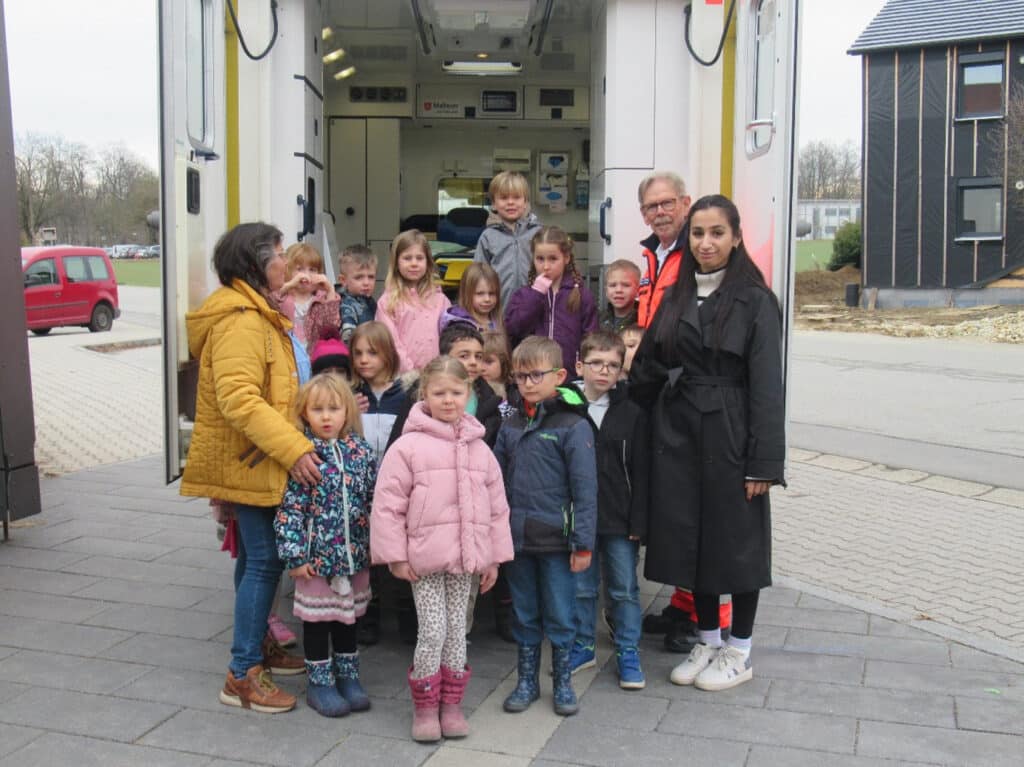 Kindergruppe vor einem Einsatzfahrzeug Eine Gruppe von Kindern steht gemeinsam mit drei Erwachsenen vor dem geöffneten Heck eines Einsatzfahrzeugs.