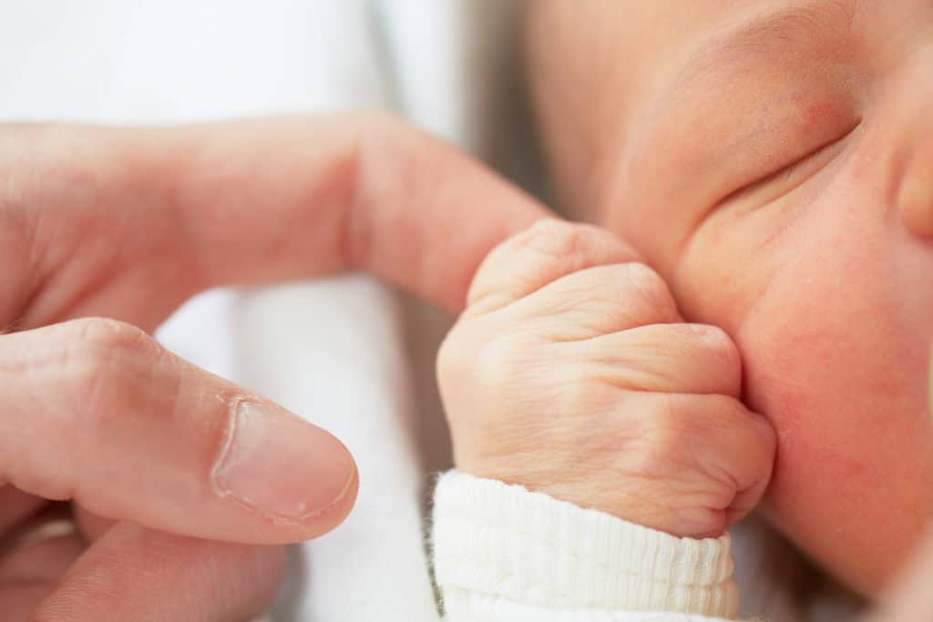 Nahaufnahme eines schlafenden Neugeborenen, das seine Hand an einen Finger eines Erwachsenen legt.