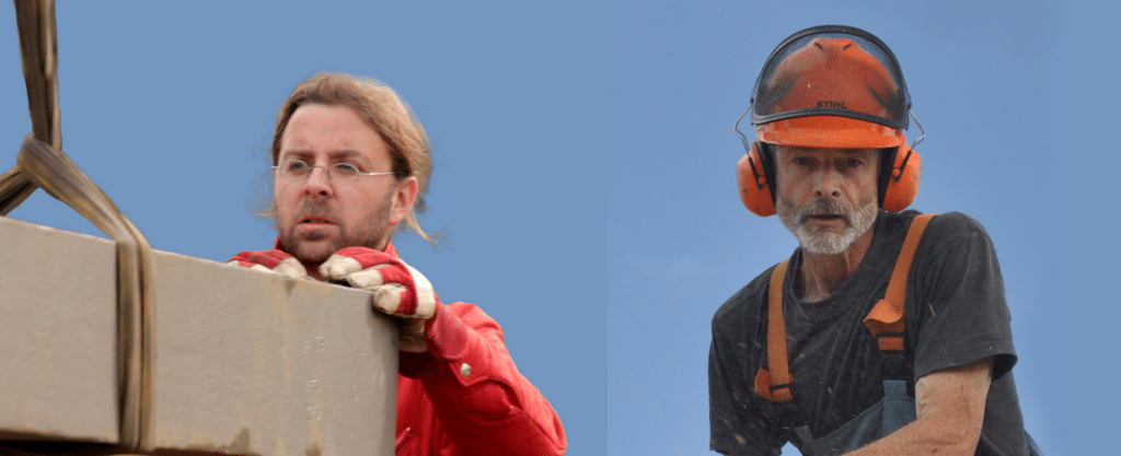 Zwei Männer blicken über eine große Kiste; links ein Mann mit Brille und roter Jacke, rechts ein Mann mit Schutzhelm und Gehörschutz.