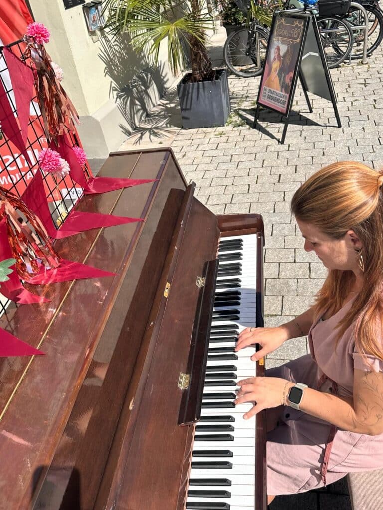 Eine Frau spielt im Freien auf einem dekorierten Klavier in der Deggendorfer Innenstadt.