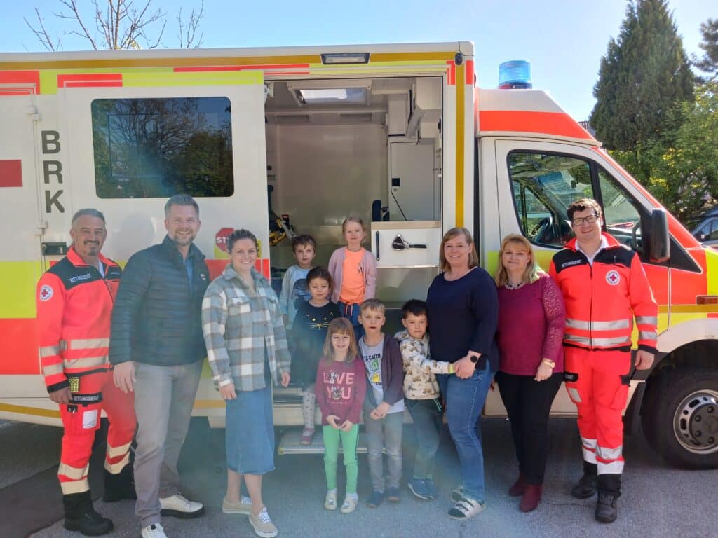 Hafenbrädl bei einer Veranstaltung mit dem Bayerischen Roten Kreuz Eine Gruppe aus Erwachsenen und Kindern steht vor einem Rettungswagen des Bayerischen Roten Kreuzes.