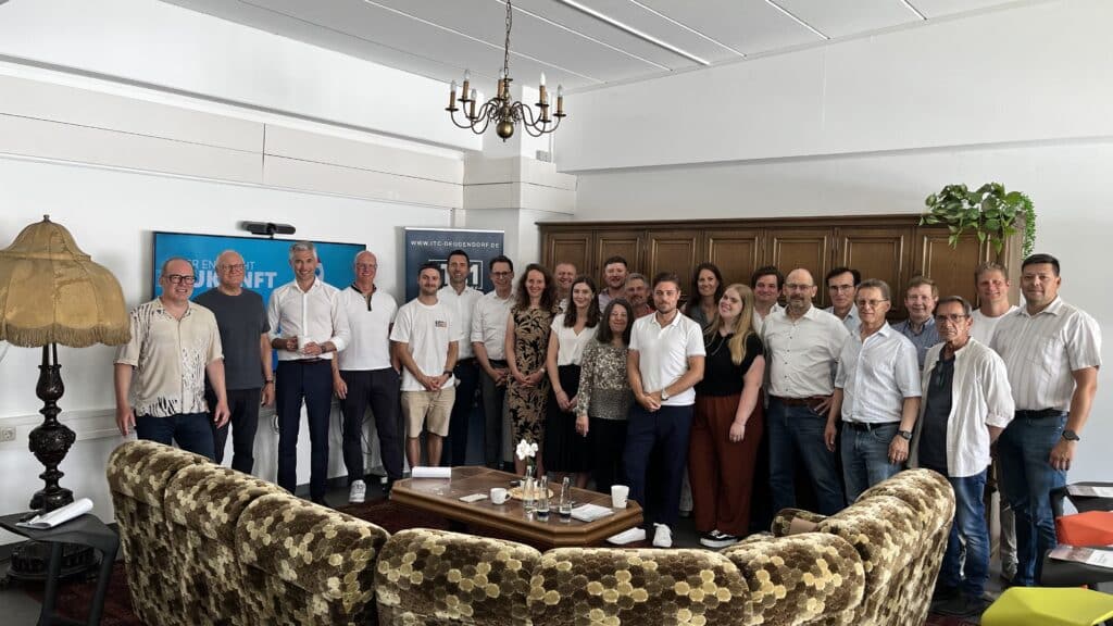 Gruppenfoto der Teilnehmenden der UT-Veranstaltung in Landau Gruppe von etwa 25 Erwachsenen posiert in einem repräsentativen Raum mit Kronleuchter, Holztäfelung und Sitzgruppe.
