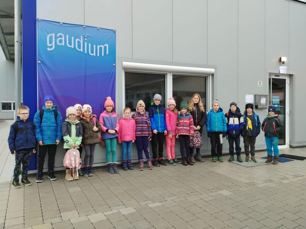 Gruppe von Kindern und Jugendlichen steht vor dem Eingang des Gaudium-Gebäudes; hinter ihnen hängt ein großes Gaudium-Banner.