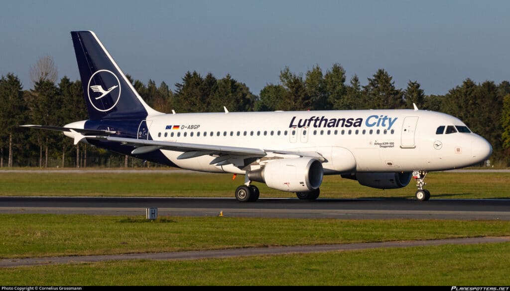 Lufthansa City Airlines Airbus A319 auf der Start- und Landebahn Ein Airbus A319 der Lufthansa City Airlines rollt auf einer Start- und Landebahn; im Hintergrund sind Bäume zu sehen.