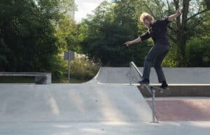 Skateboarder balanciert auf einem Geländer in einem von Bäumen umgebenen Skatepark.