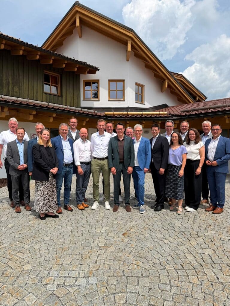 Gruppenfoto von rund 20 Personen vor einem traditionellen Gebäude auf einem gepflasterten Platz.
