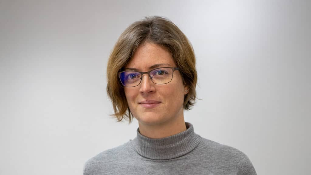 Porträt einer Frau mit kurzen braunen Haaren und Brille vor hellem Hintergrund