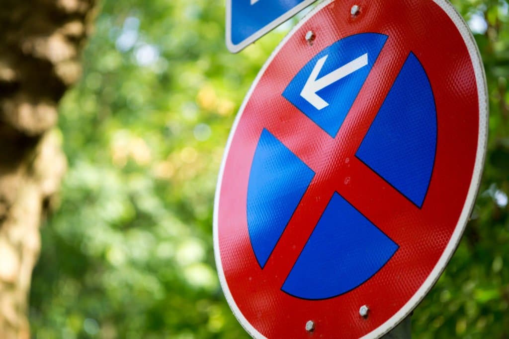 Nahaufnahme eines Verkehrszeichens für ein beidseitiges Halt- und Parkverbot an einem von Bäumen gesäumten Straßenrand