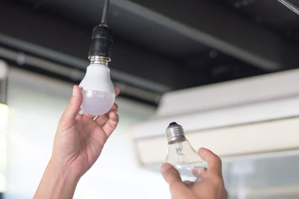 Zwei Hände halten eine herkömmliche und eine transparente LED-Glühbirne zum Vergleich.