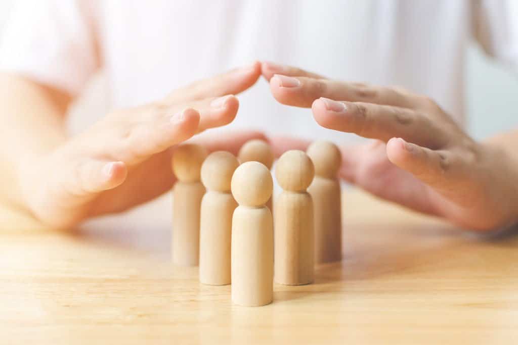 Hände schützen eine Gruppe hölzerner Figuren auf einem Tisch.